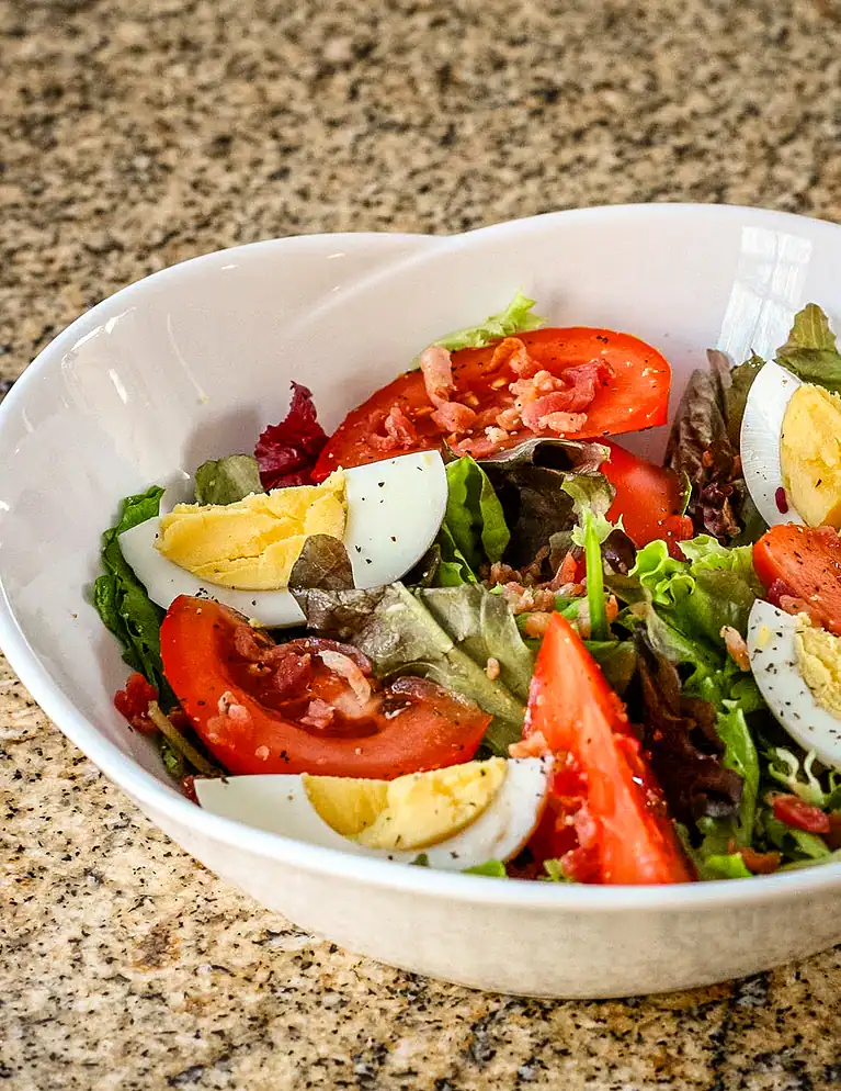 Fresh garden salad with tomatoes, boiled eggs, and bacon bits.