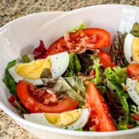 A bowl with a simple blt salad with tomatoes, hard-boiled eggs, lettuce, and bacon.