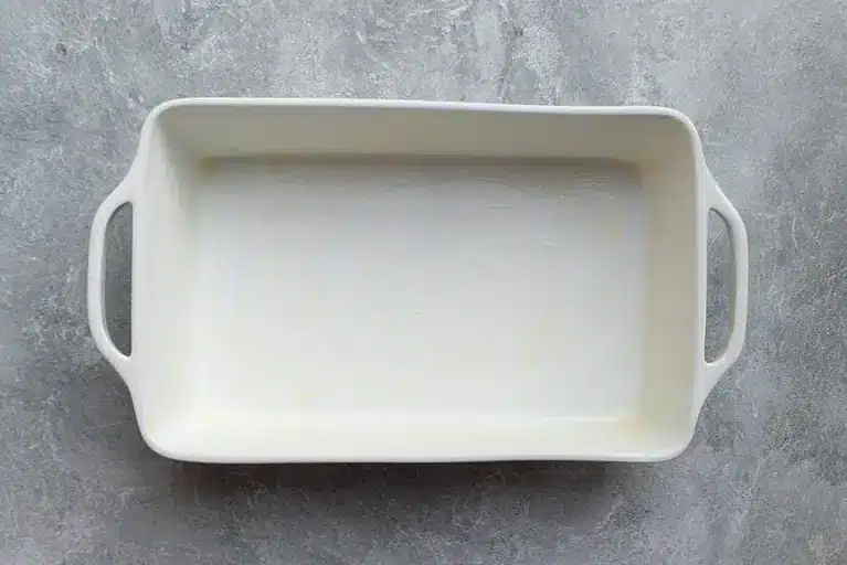 Empty white rectangular baking dish with handles on a textured gray surface.