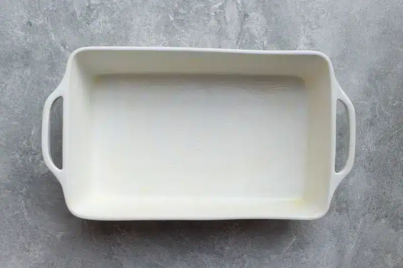 Empty white rectangular baking dish with handles on a textured gray surface.