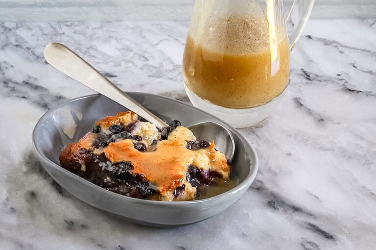 Sweet blueberry cobbler with a side of creamy gravy in a gray dish.