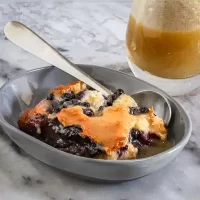 Creamy blueberry cobbler topped with melted cheese and served in a gray dish.