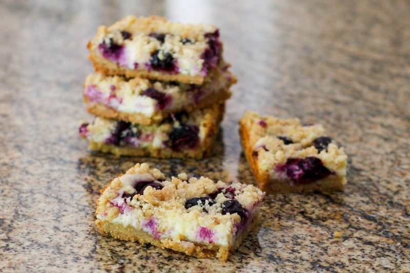 blueberry cheesecake bars with cream cheese filling, stacked on the countertop