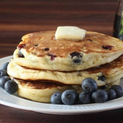 fluffy blueberry pancakes on a plate with butter and fresh blueberries