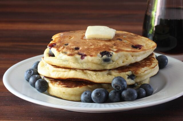 fluffy blueberry pancakes on a plate with butter and fresh blueberries