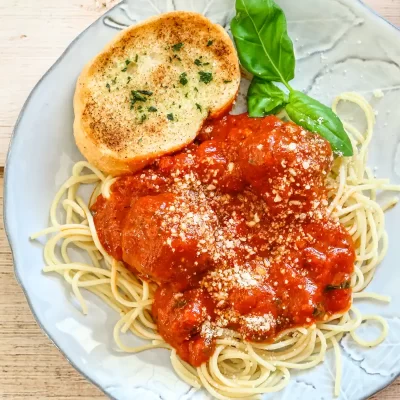 Plate of spaghetti with tomato sauce, topped with cheese and served with garlic bread and basil.