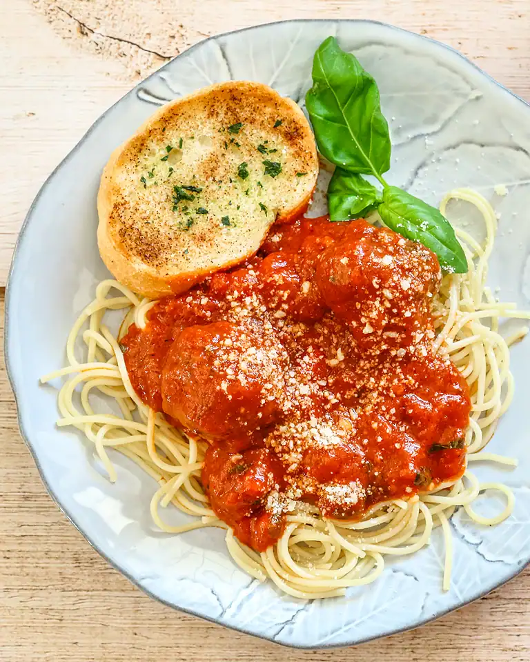 Plate of spaghetti with tomato sauce, topped with cheese and served with garlic bread and basil.
