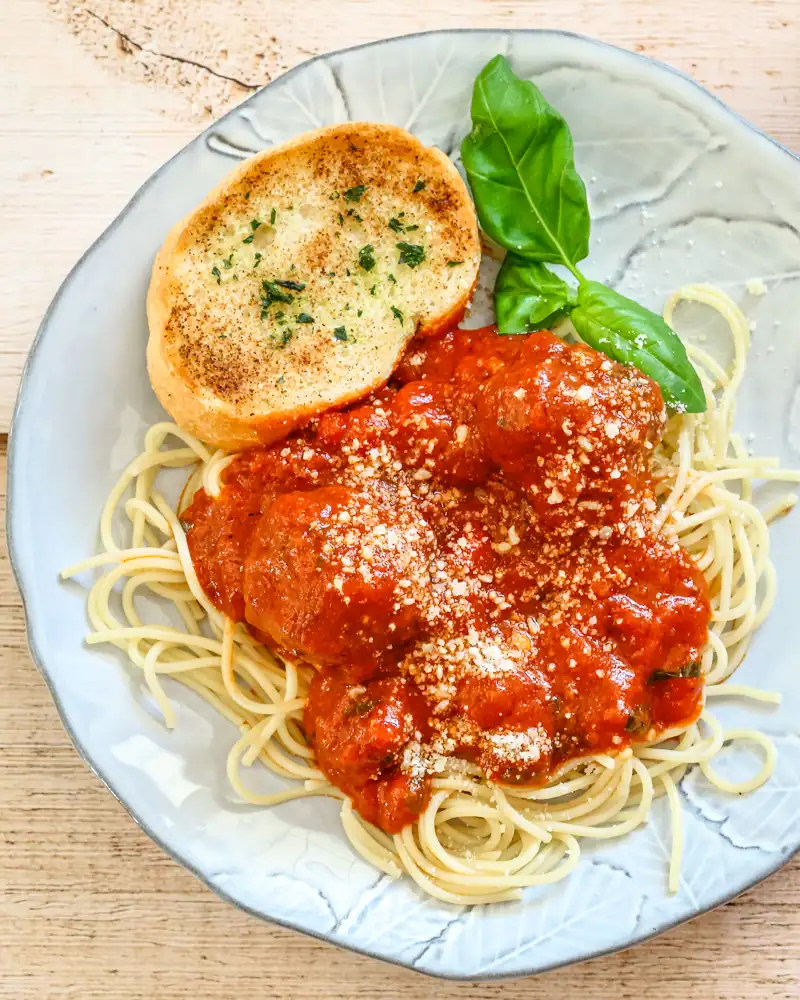 Plate of spaghetti with tomato sauce, topped with cheese and served with garlic bread and basil.