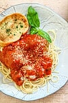 Freshly cooked spaghetti topped with marinara sauce and grated cheese, garnished with basil, with a slice of garlic bread on a decorative plate.