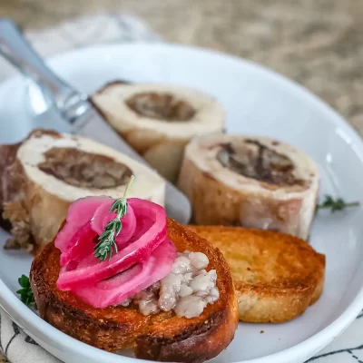Roasted bone marrow serving with pickled onions and toasted bread slices.
