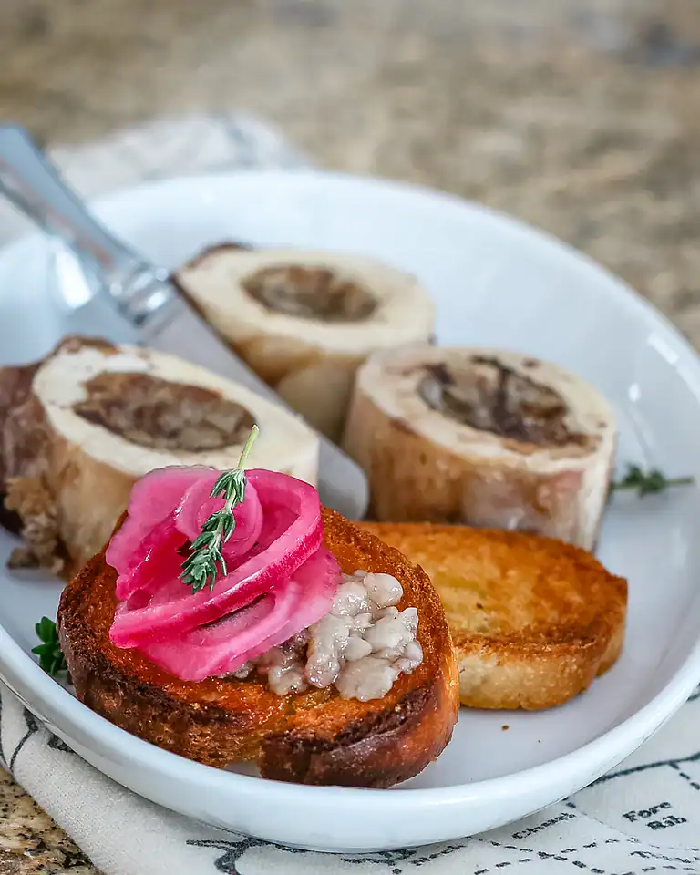 Roasted bone marrow serving with pickled onions and toasted bread slices.