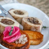 A bone marrow appetizer with crostini, thyme, and pickled red onions.