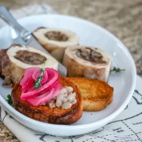 Fried bread topped with pickled onions and herbs on a white plate.