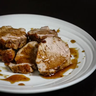 Succulent sliced roast pork drizzled with gravy on a white plate.