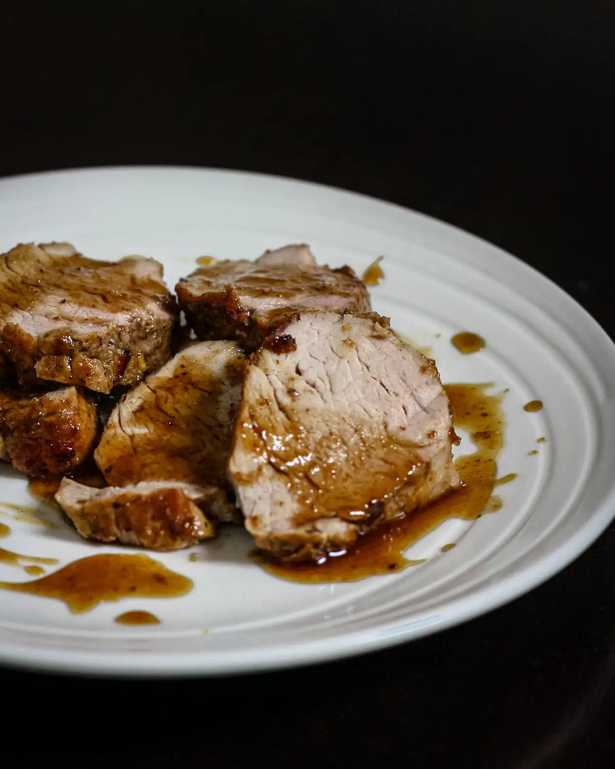 Succulent sliced roast pork drizzled with gravy on a white plate.