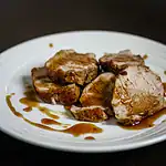 Roast pork loin slices with gravy on white plate.