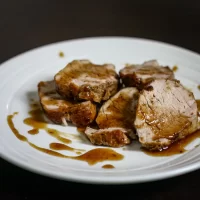 Roast pork loin slices with gravy on white plate.