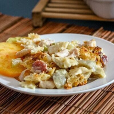 bowtie pasta is shown on a plate with creamy fontina cheese sauce, ham, and sliced tomatoes.