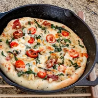 Golden brown pizza with cherry tomatoes, fresh basil, and melted cheese in a cast iron skillet.