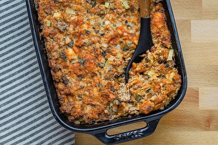 Brioche stuffing in a baking dish with sausage, herbs, and aromatics.