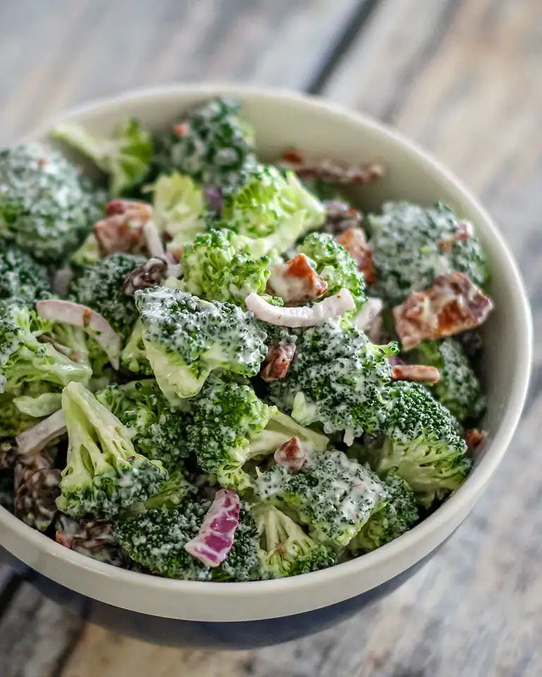 Creamy broccoli salad with red onion and bacon bits.
