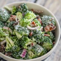 A serving bowl with broccoli crunch salad featuring bacon, raisins, and red onions.
