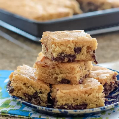 Golden chocolate chip cookie bars stacked on a plate.