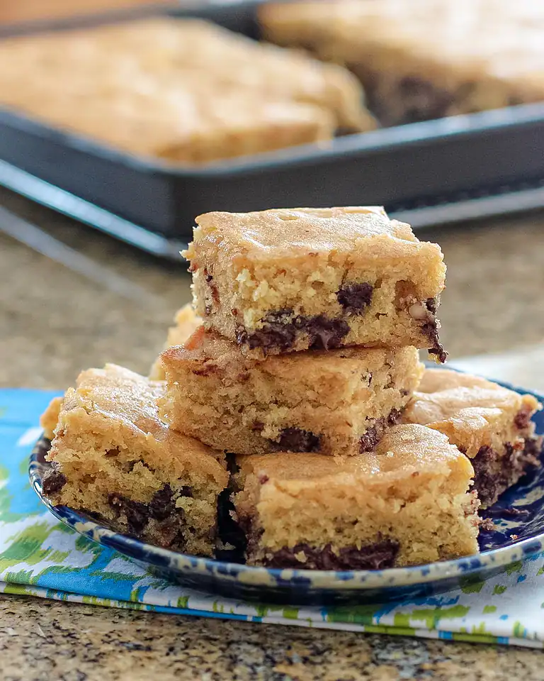 Golden chocolate chip cookie bars stacked on a plate.
