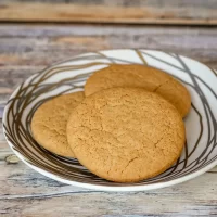 Golden chocolate chip cookies in a patterned bowl on a rustic wooden surface.