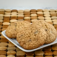 Chewy chocolate chip cookies on a white plate against a wooden background.