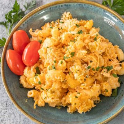 Buffalo chicken mac and cheese on a plate with some parsley and grape tomatoes.