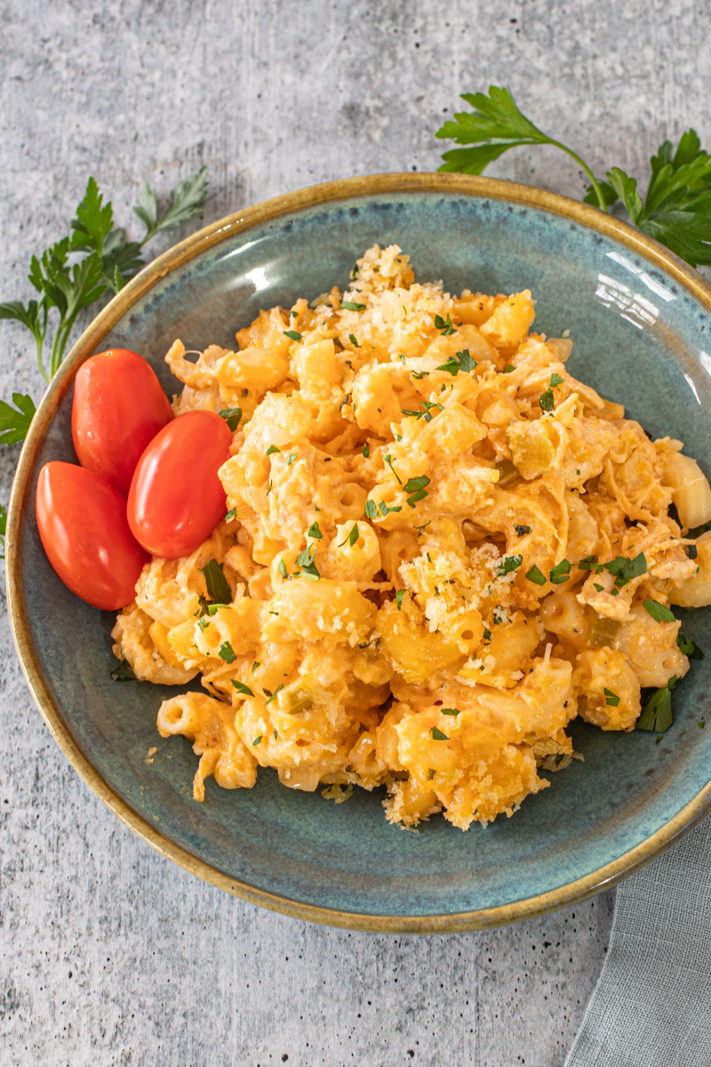 Buffalo chicken mac and cheese on a plate with some parsley and grape tomatoes.