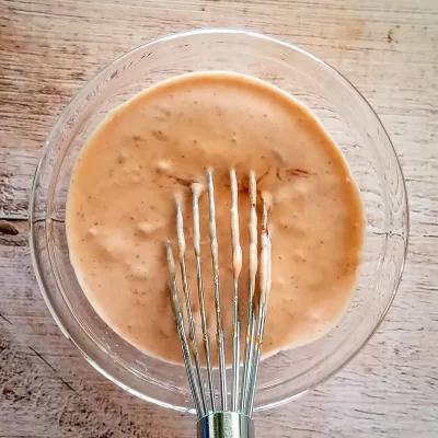 Creamy salad dressing mixed in a glass bowl with a whisk.