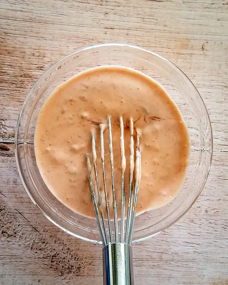 Creamy salad dressing mixed in a glass bowl with a whisk.