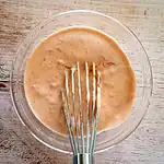 Creamy salad dressing mixed with a fork in a glass bowl.