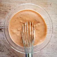 Creamy salad dressing mixed with a fork in a glass bowl.