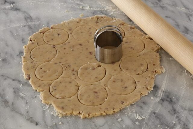 Cutting out butter pecan cookies with a small round cookie cutter.