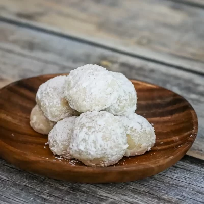Fresh coconut cookies dusted with powdered sugar on a wooden plate.