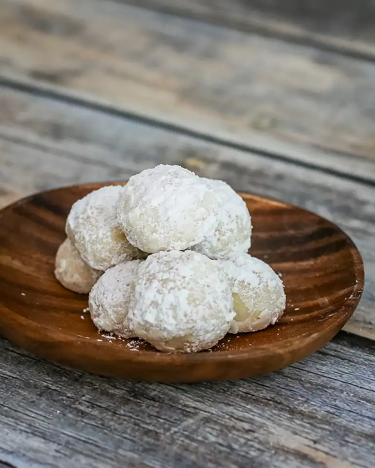 Fresh coconut cookies dusted with powdered sugar on a wooden plate.
