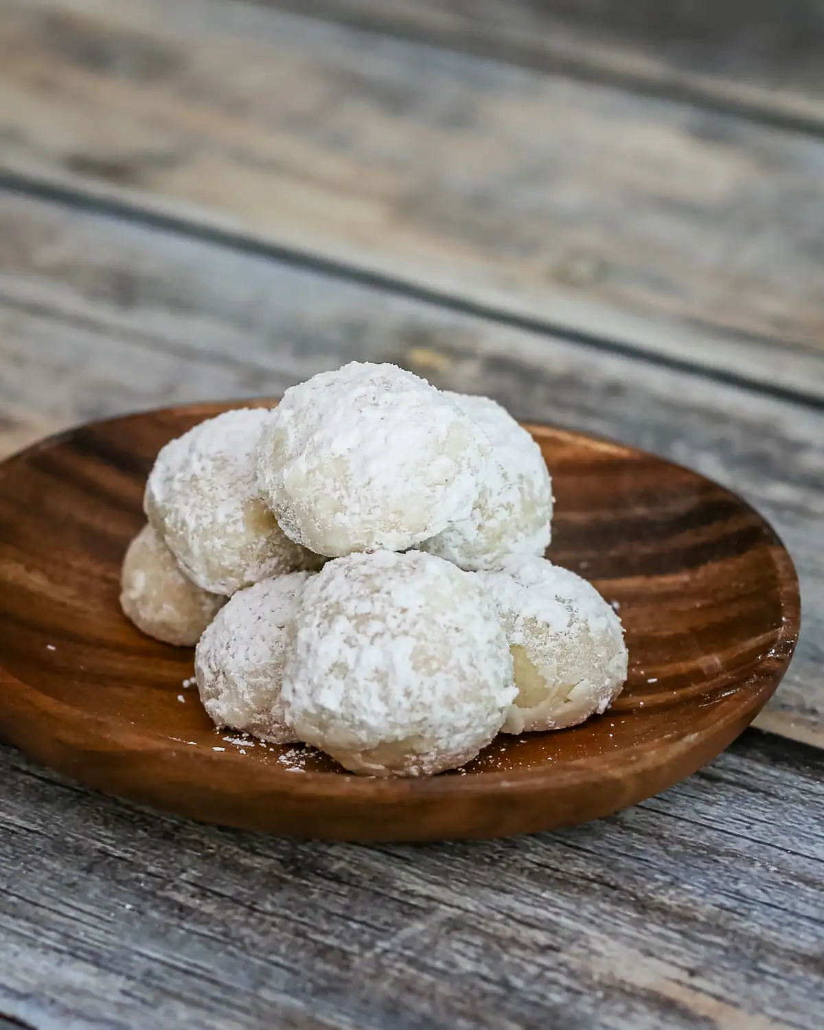 Fresh coconut cookies dusted with powdered sugar on a wooden plate.