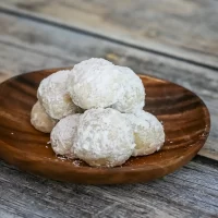 Cookies dusted with powdered sugar on a wooden plate.