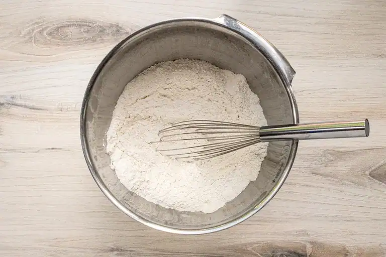 Flour and dry ingredients in a stainless steel mixing bowl with whisk.