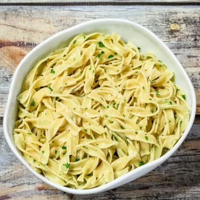 Creamy garlic pasta with parsley in a white bowl on rustic wooden surface.