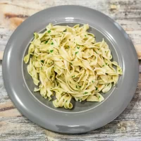 Fettuccine pasta garnished with chopped parsley on a gray plate.