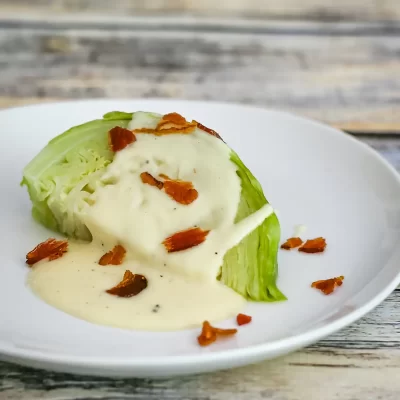 Baked lettuce wrapped with creamy sauce and crispy bacon bits on a white plate.