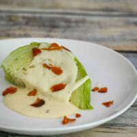 Cabbage wedge on a plate with cheese sauce and crispy bacon.