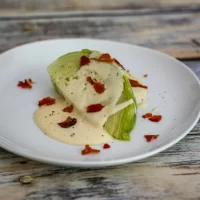 Creamy lettuce wedge topped with bacon bits on white plate.