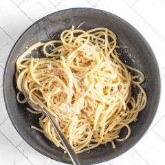 A bowl of cacio e pepe pasta with fresh grated Parmesan cheese and a fork.