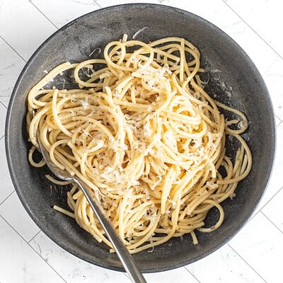 A bowl of cacio e pepe pasta with fresh grated Parmesan cheese and a fork.