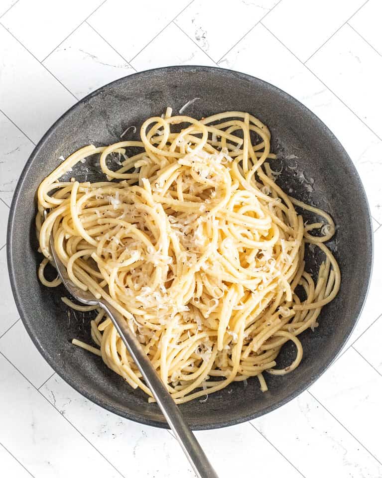 A bowl of cacio e pepe pasta with fresh grated Parmesan cheese and a fork.